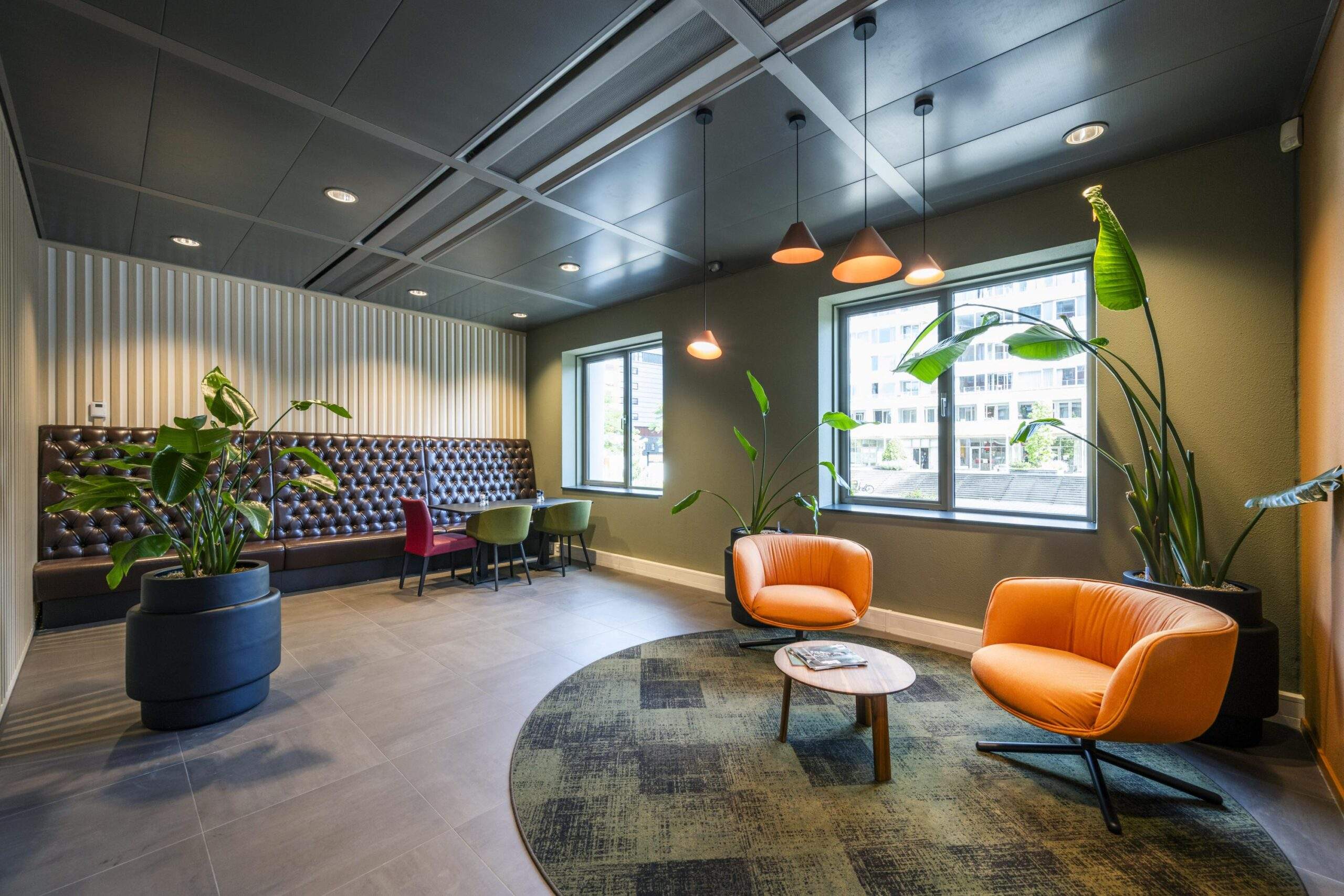 Moderne wachtruimte aan het Koningin Wilhelminaplein met oranje fauteuils, grote planten en stijlvolle verlichting.